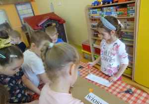 Dzieci przygotowują plakat, naklejają napis na duży arkusz papieru.